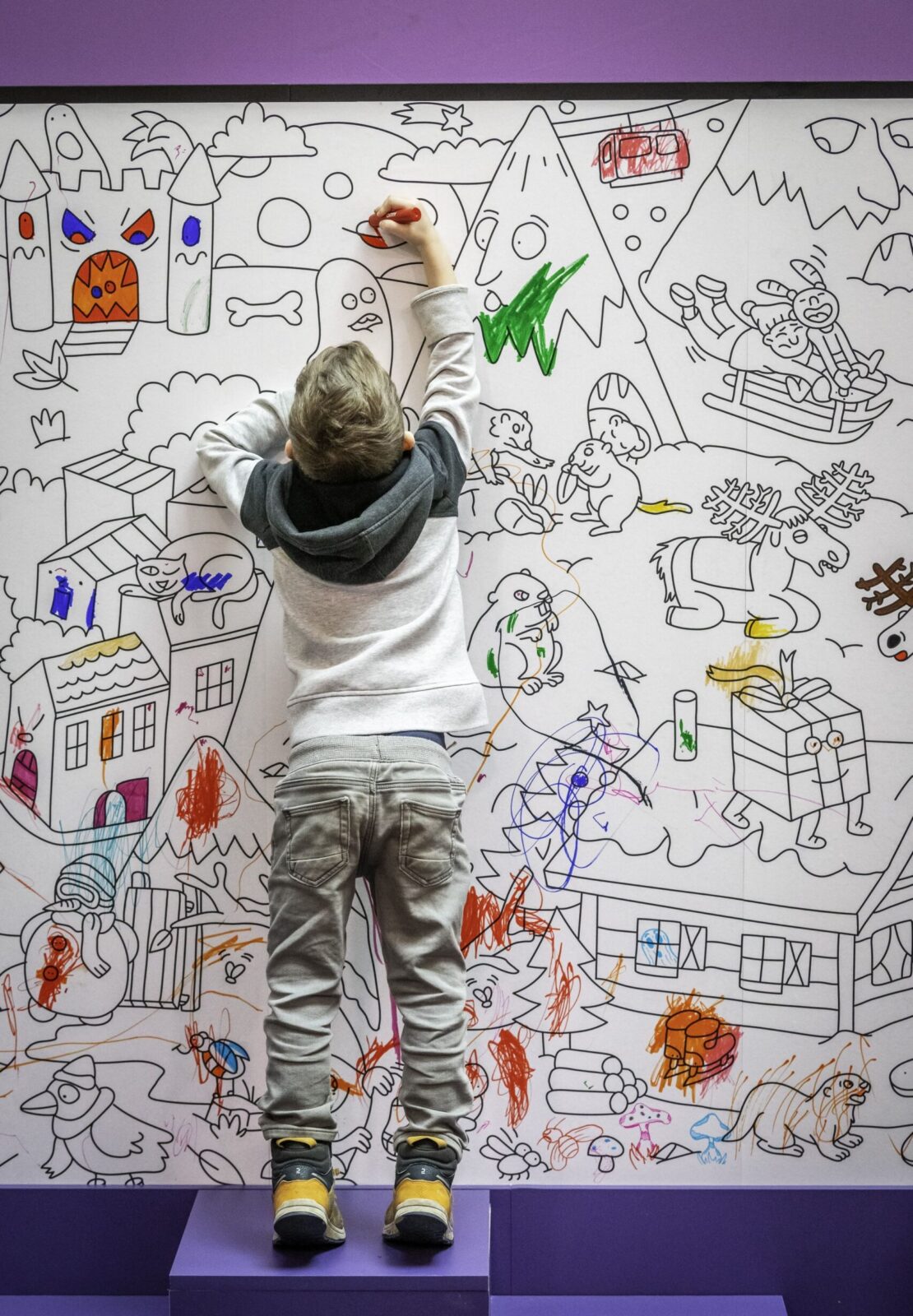 A child interacting with a large illustrated wall by coloring playful scenes, highlighting the hands-on and educational approach of the Action Innocence traveling pavilion designed to encourage learning through creativity and engagement.