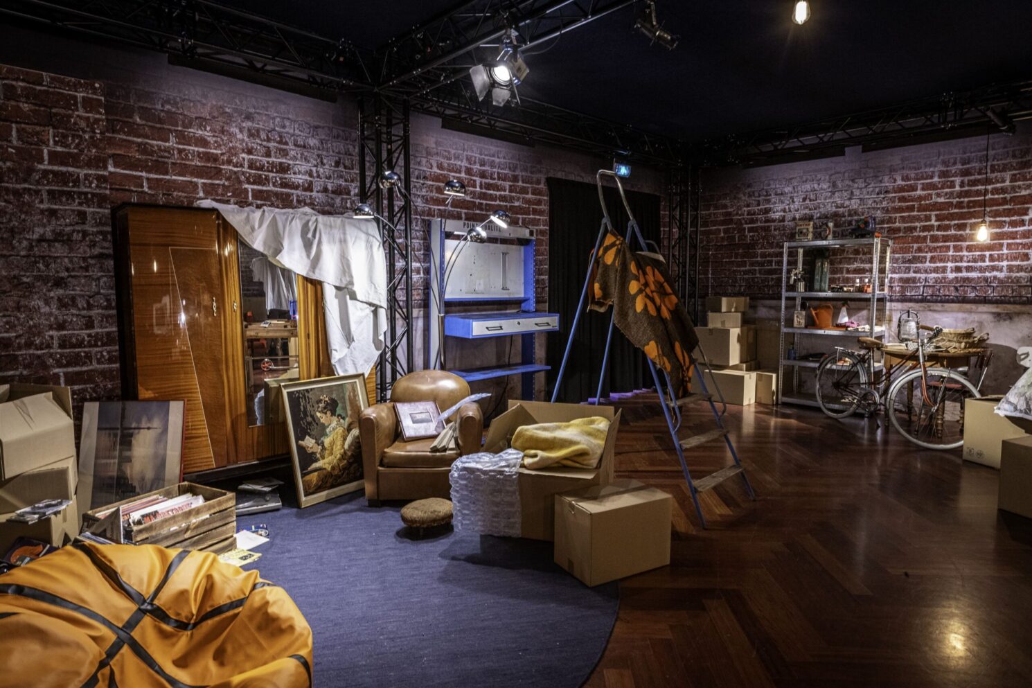 A detailed interior scene of the Action Innocence traveling educational pavilion, designed as an immersive domestic setting with furniture, personal objects, and staged lighting to spark discussion about online behavior, privacy, and digital life in everyday environments.