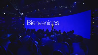 Speaker welcoming the audience on stage in front of a large blue screen reading “Bienvenidos” during the Conference in Buenos Aires – Immersive 360°.
