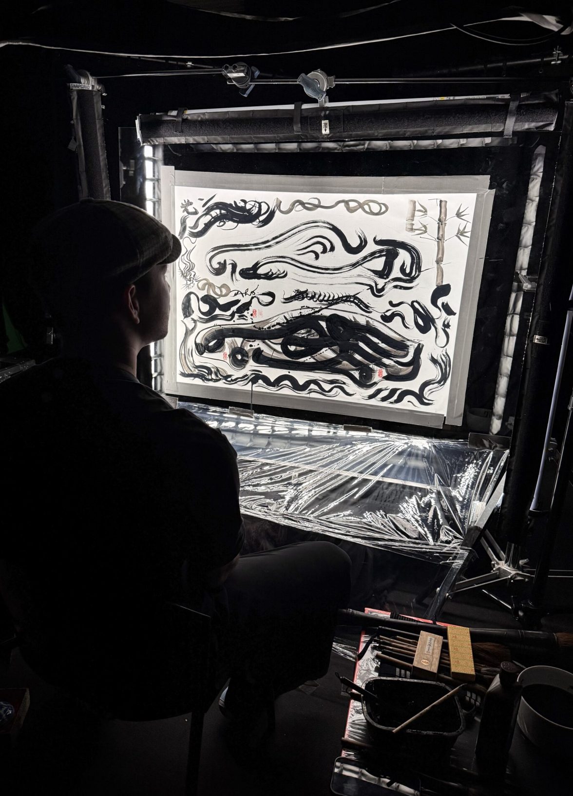 Artist observing a large ink artwork inside a backstage setup during the Mazda – Cinematic reveal of the Mazda 6E.