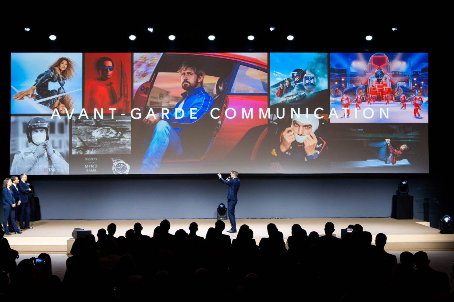 Speaker presenting on stage in front of a large screen displaying “Avant-Garde Communication” during Watches & Wonders – Geneva International Watchmaking Exhibition.